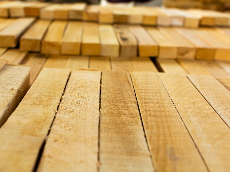 Close-up of stacked light-colored beechwood planks with visible grain and seams, photographed in a workshop or lumber setting.