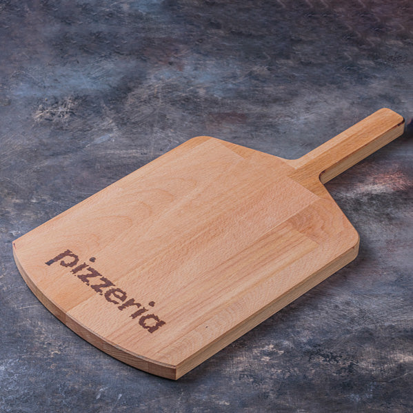 A wooden pizza peel with a handle, featuring the word 'pizzeria' engraved on the side, set against a dark textured slate background.