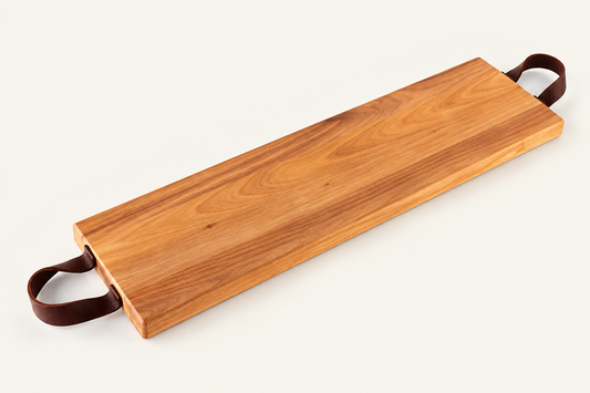 A rectangular wooden serving board with a warm honey-brown wood grain and dark brown leather handles on both ends, shown on a clean off-white background.