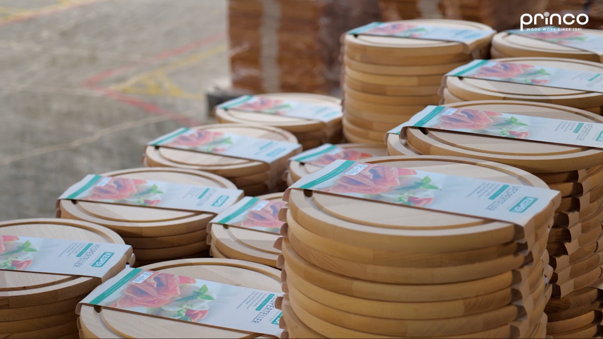 Stacks of round wooden cutting boards with floral paper bands, displayed outdoors on a concrete surface. The brand name 'princo' is visible in the top right corner.