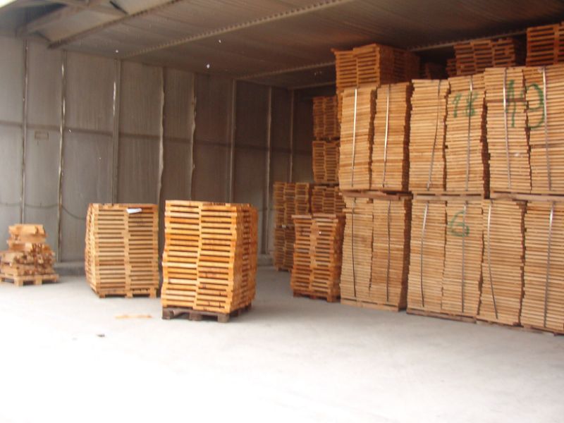 Stacks of wooden pallets in varying sizes stored inside a warehouse or storage facility with concrete floors and corrugated metal walls.